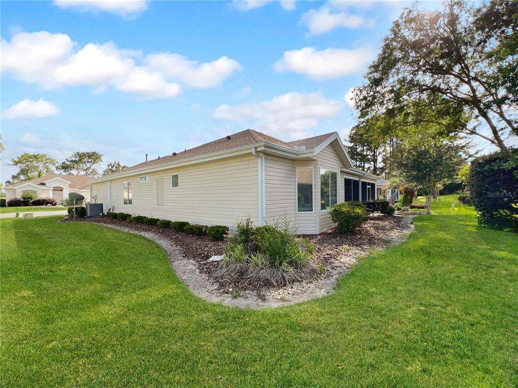 The side exterior of a beige, single-story house with a screened-in porch and landscaping — 13150 SE 93RD CIRCLE, SUMMERFIELD, FL