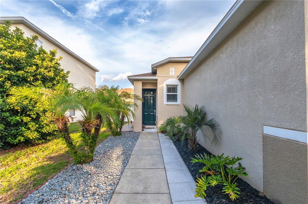A concrete walkway leads to the front door of a house with beige stucco siding — 9644 SIMEON DRIVE, LAND O LAKES, FL