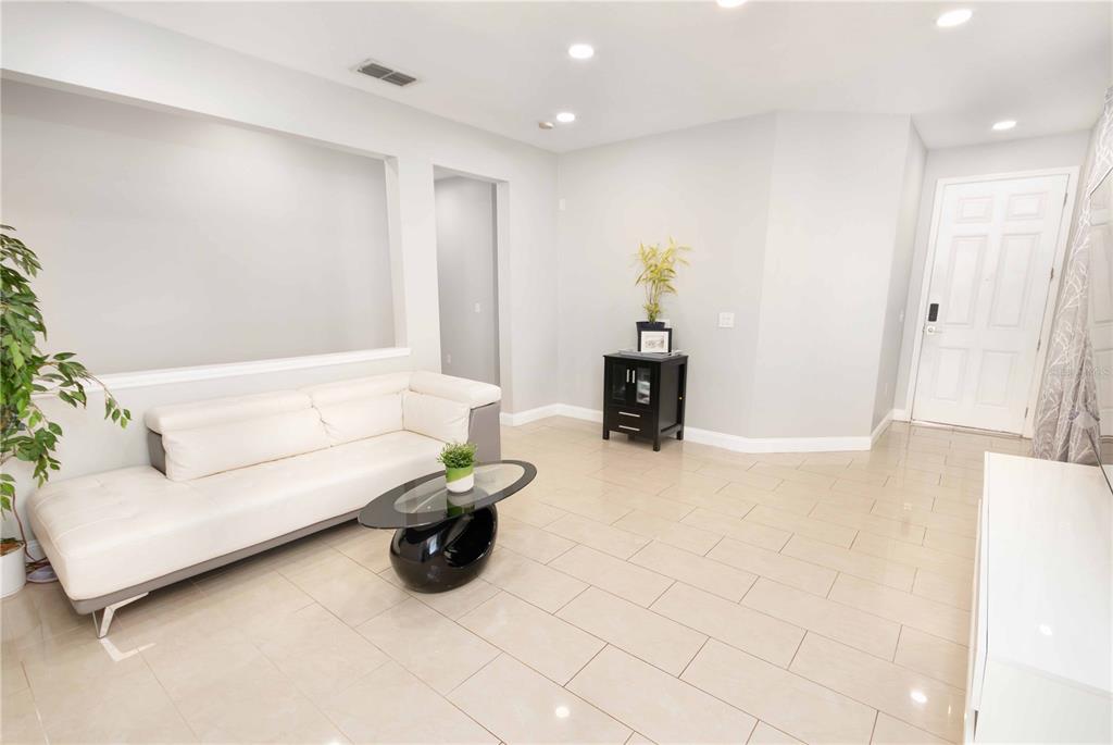 A living room features a white sofa, a glass coffee table, and light tile flooring — 9644 SIMEON DRIVE, LAND O LAKES, FL