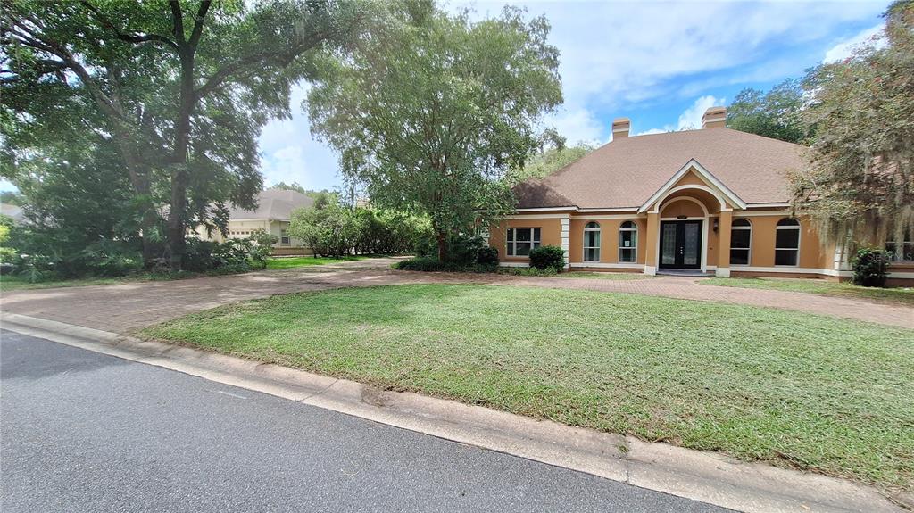 A tan single-story house with a brick driveway and large trees in the front yard — 2210 SE LAUREL RUN DRIVE, OCALA, FL