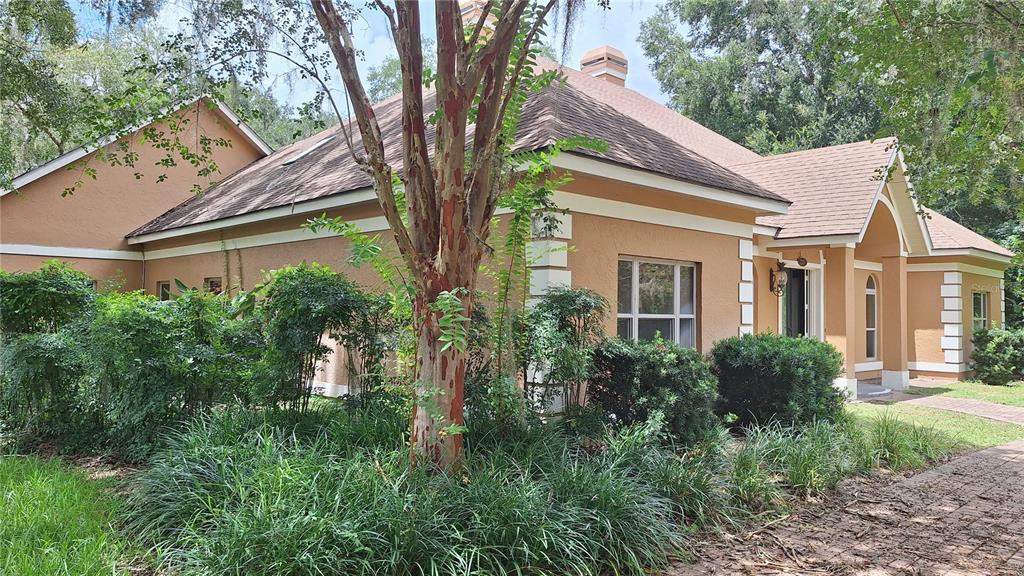 A tan stucco house with a brown shingled roof is surrounded by trees and landscaping — 2210 SE LAUREL RUN DRIVE, OCALA, FL