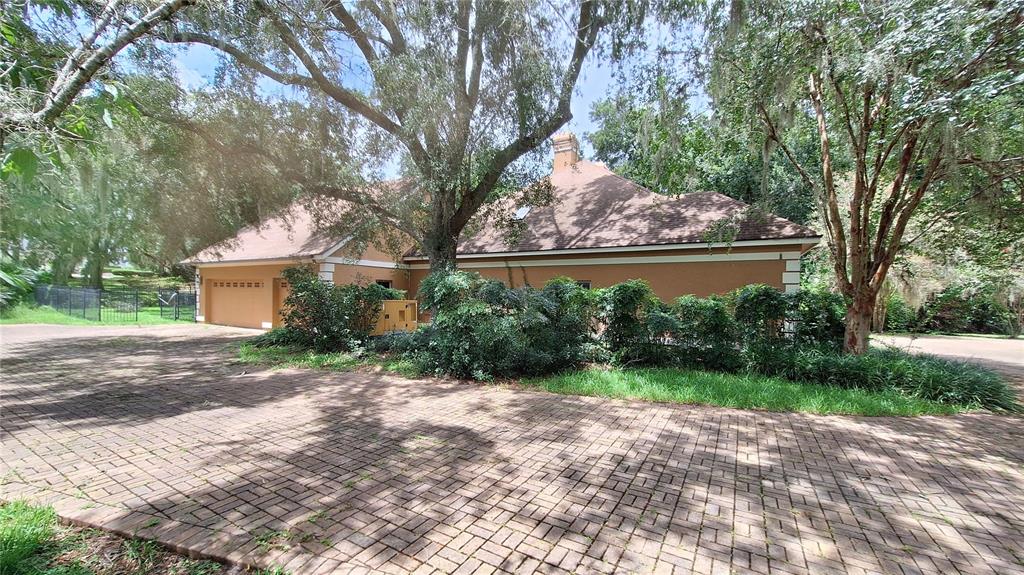 A tan house with a brown roof and brick driveway surrounded by large oak trees — 2210 SE LAUREL RUN DRIVE, OCALA, FL