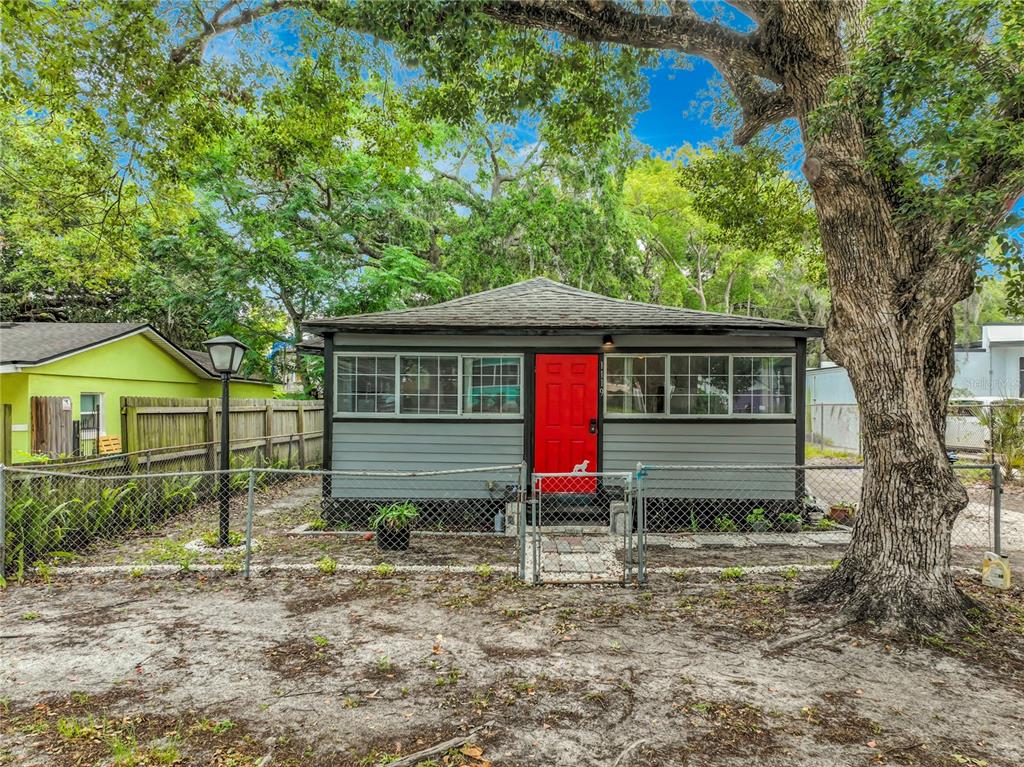 A small, gray, single-story house with a bright red front door and a chain-link fence — 1119 CYPRESS AVENUE, SANFORD, FL
