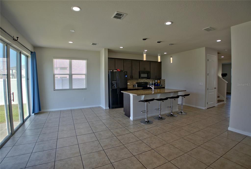 A kitchen with dark cabinets and a granite island overlooks an open-concept tiled living area — 3576 BRISTOL COVE LANE, ST CLOUD, FL