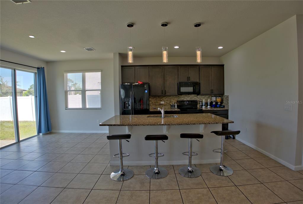 A kitchen features dark cabinets, granite countertops, a central island with barstools, and tile flooring — 3576 BRISTOL COVE LANE, ST CLOUD, FL