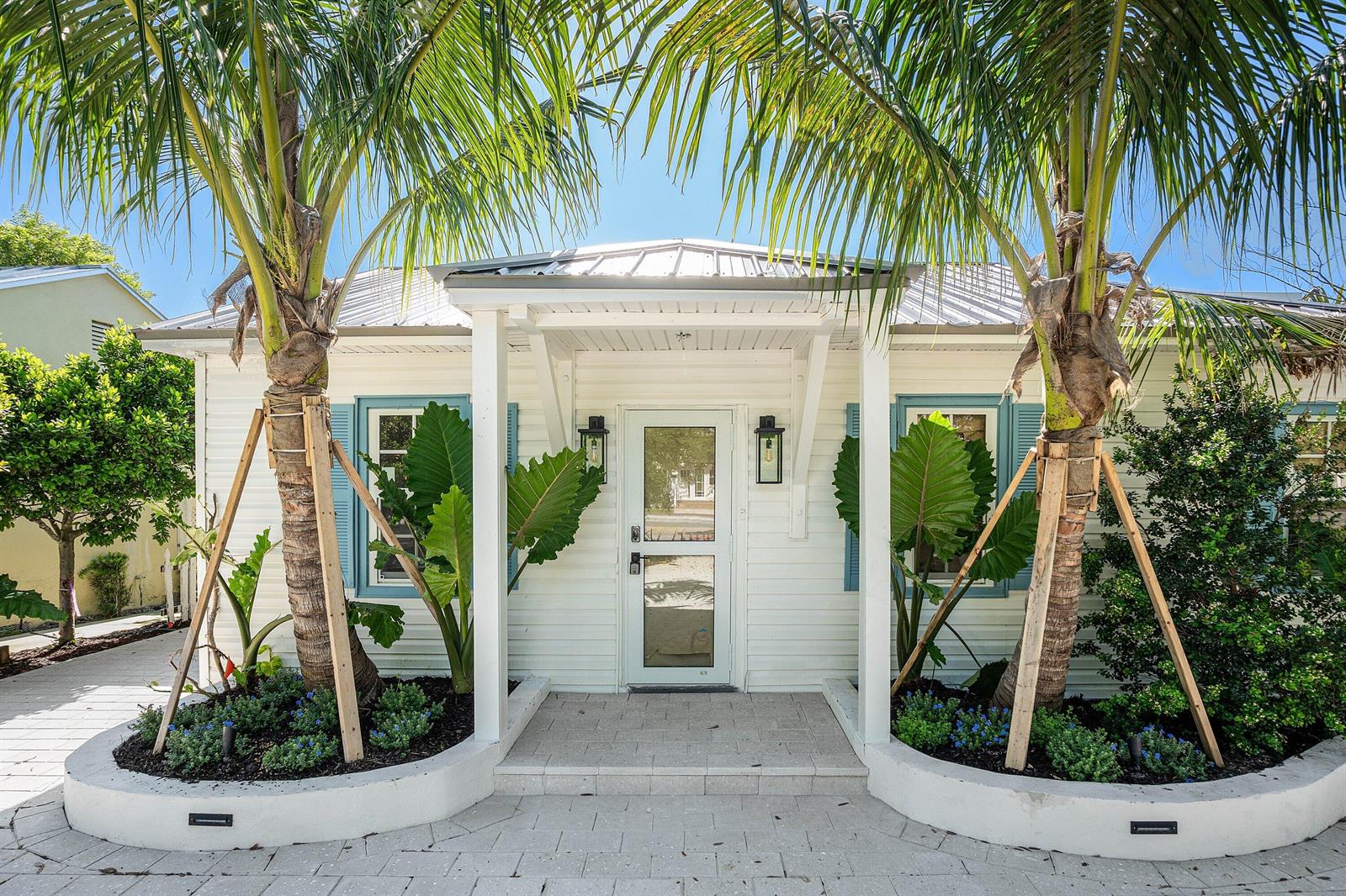A white cottage exterior features a covered entryway, two palm trees, and blue window shutters — 23 S Swinton Avenue, Delray Beach FL 33444, DELRAY BEACH, FL