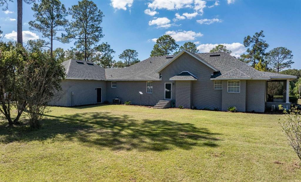 The rear exterior of a single-story brick house features a lawn and surrounding trees — 1237 SW OLD LAKE CITY TERRACE, HIGH SPRINGS, FL