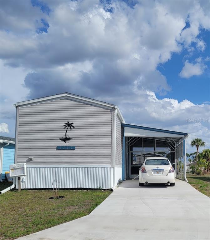 A light gray manufactured home with a white carport and a palm tree wall decoration — 5700 HOLIDAY PARK BOULEVARD, NORTH PORT, FL