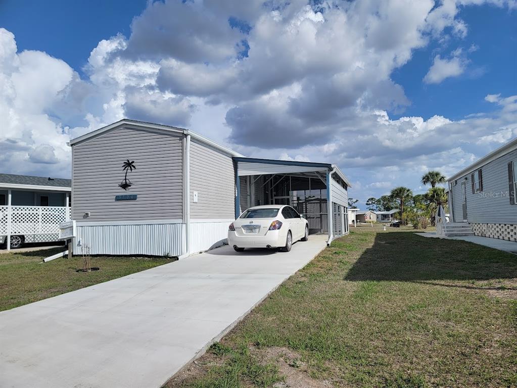 A light gray mobile home features a concrete driveway, a carport, and a palm tree decal — 5700 HOLIDAY PARK BOULEVARD, NORTH PORT, FL