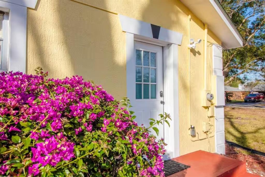 A yellow house exterior features a white door, a red stoop, and a large bougainvillea bush — 3120 PEEL AVENUE UNIT 2, ORLANDO, FL