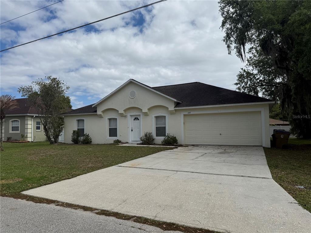 A single-story house with a beige stucco exterior, a two-car garage, and a concrete driveway — 405 FRANCISCO WAY, KISSIMMEE, FL