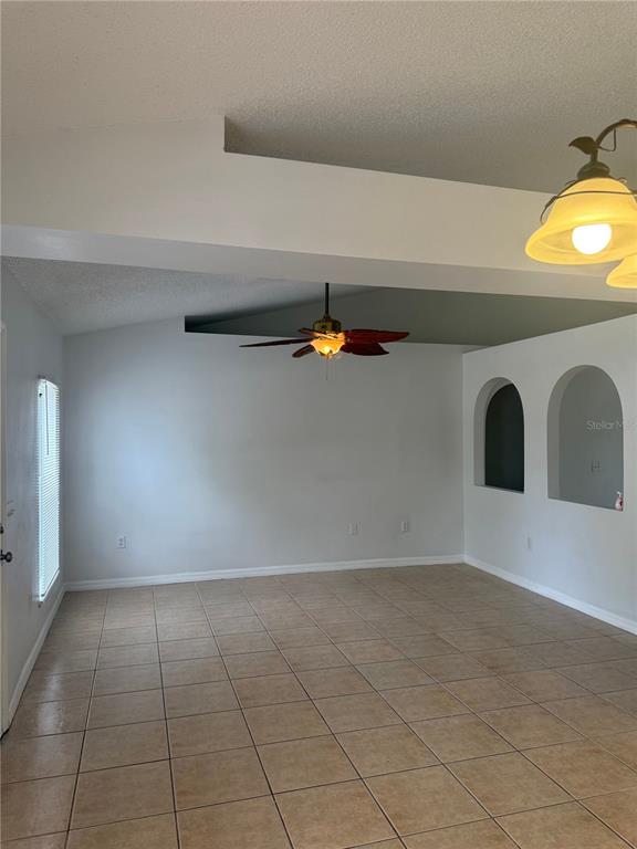 An empty room features light-colored tile flooring, a ceiling fan, and two arched wall cutouts — 405 FRANCISCO WAY, KISSIMMEE, FL