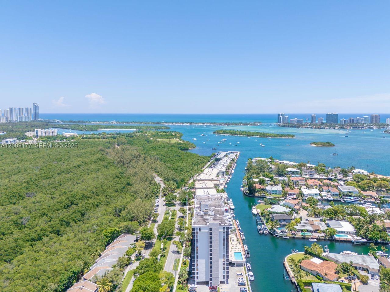 An aerial view shows a tall residential building situated between a dense forest and a canal — 2500 NE 135th St # C1011, North Miami FL 33181, NORTH MIAMI, FL
