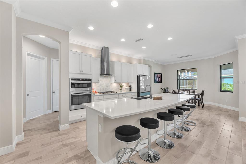 A modern kitchen features white cabinetry, a large quartz island with bar stools, and tile flooring — 814 TIRANO WAY, SUN CITY CENTER, FL