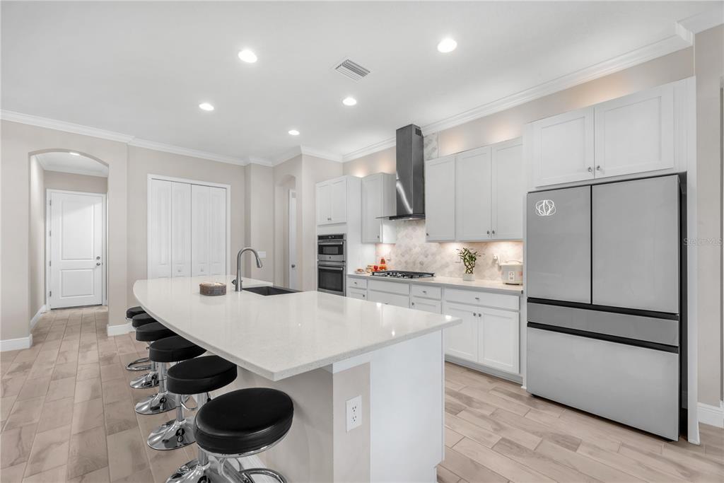 A modern kitchen features white cabinetry, a large quartz island with bar stools, and stainless appliances — 814 TIRANO WAY, SUN CITY CENTER, FL