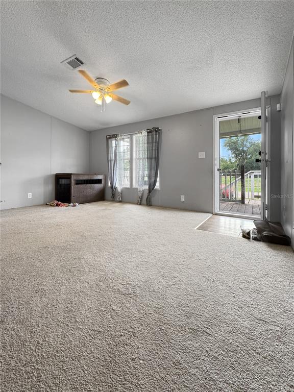 A carpeted living room features a ceiling fan, gray walls, and a door leading outside — 1113 BIG OAK DRIVE, LAKE WALES, FL