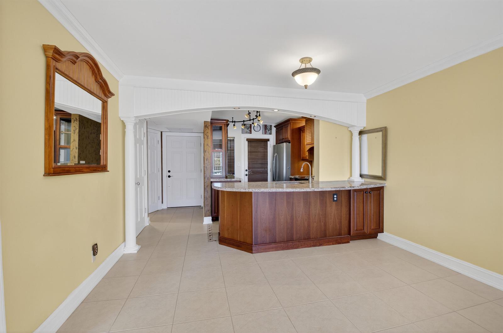 A kitchen with a granite-topped island, wooden cabinets, and a white arched entryway — 2871 N Ocean Boulevard # V247, Boca Raton FL 33431, BOCA RATON, FL