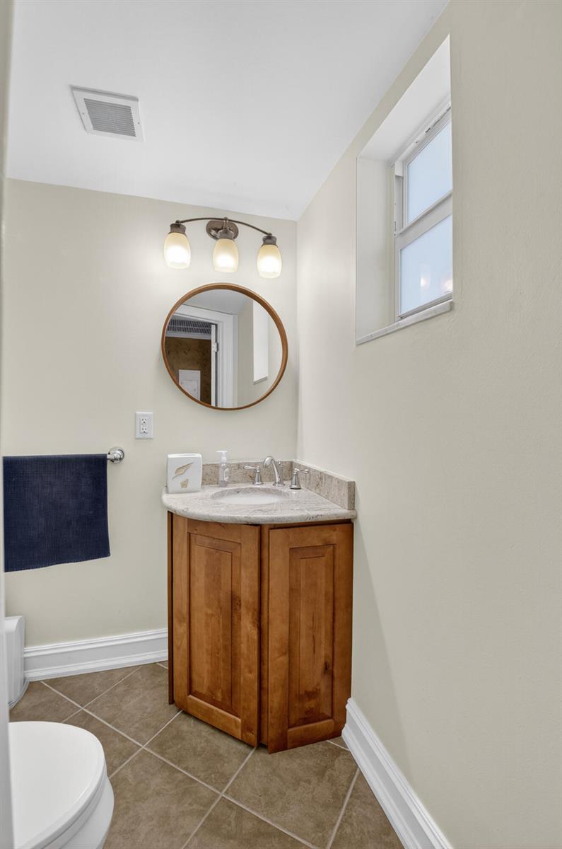 A small bathroom features a corner vanity with a granite countertop and a round mirror — 2871 N Ocean Boulevard # V247, Boca Raton FL 33431, BOCA RATON, FL
