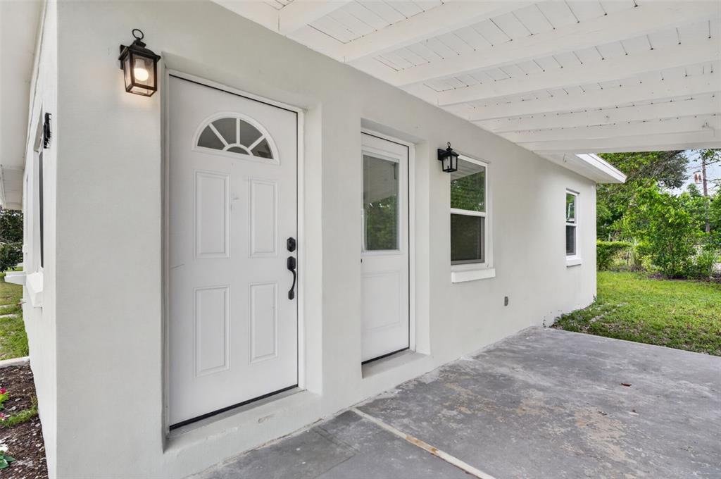 A white exterior wall features a front door, a side door, and a covered porch — 1333 STILLWATER AVE, DELTONA, FL