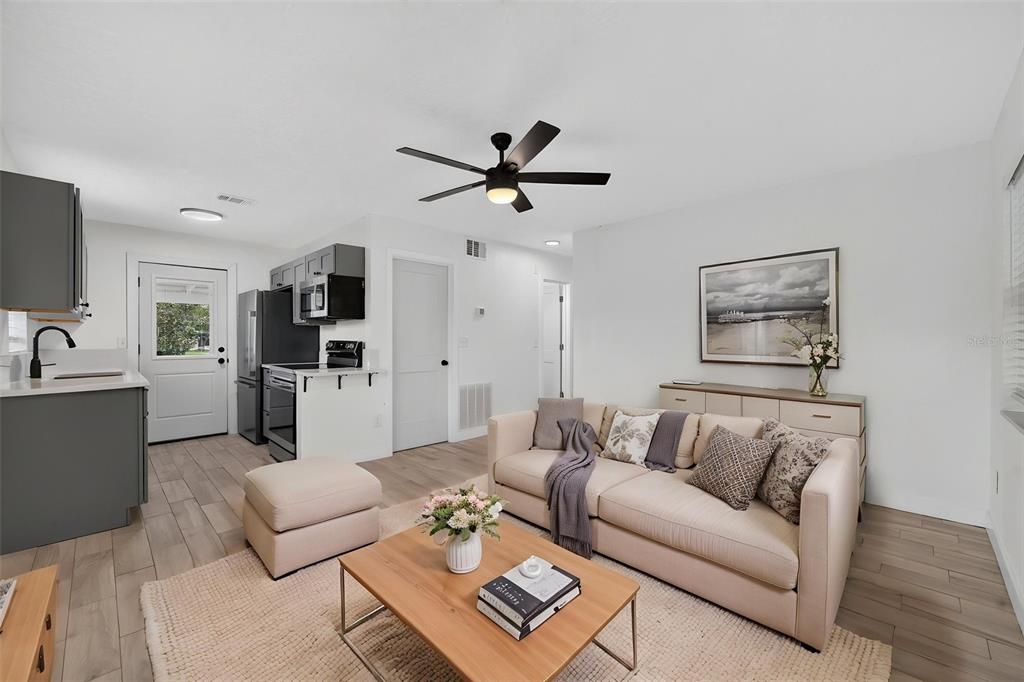 A living room with light wood-look tile floors, a beige sofa, and an open kitchen — 1333 STILLWATER AVE, DELTONA, FL
