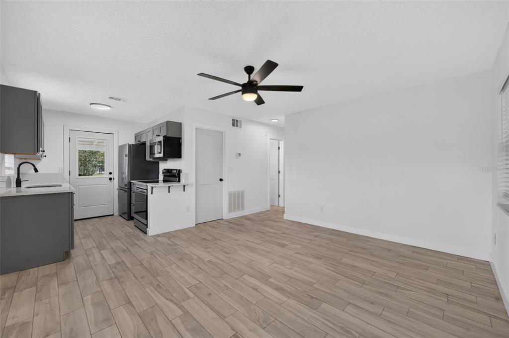 A kitchen and living area with gray cabinets, stainless steel appliances, and light wood-look flooring — 1333 STILLWATER AVE, DELTONA, FL