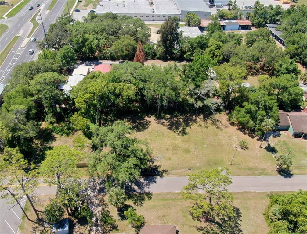 An aerial view shows a vacant, tree-lined lot situated between a road and commercial buildings — Lot 00200 LENORD STREET, UMATILLA, FL