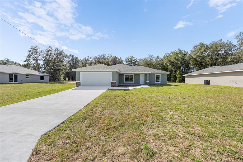 A single-story house with a two-car garage and a concrete driveway sits on a lawn — 8955 SW 139TH STREET, OCALA, FL