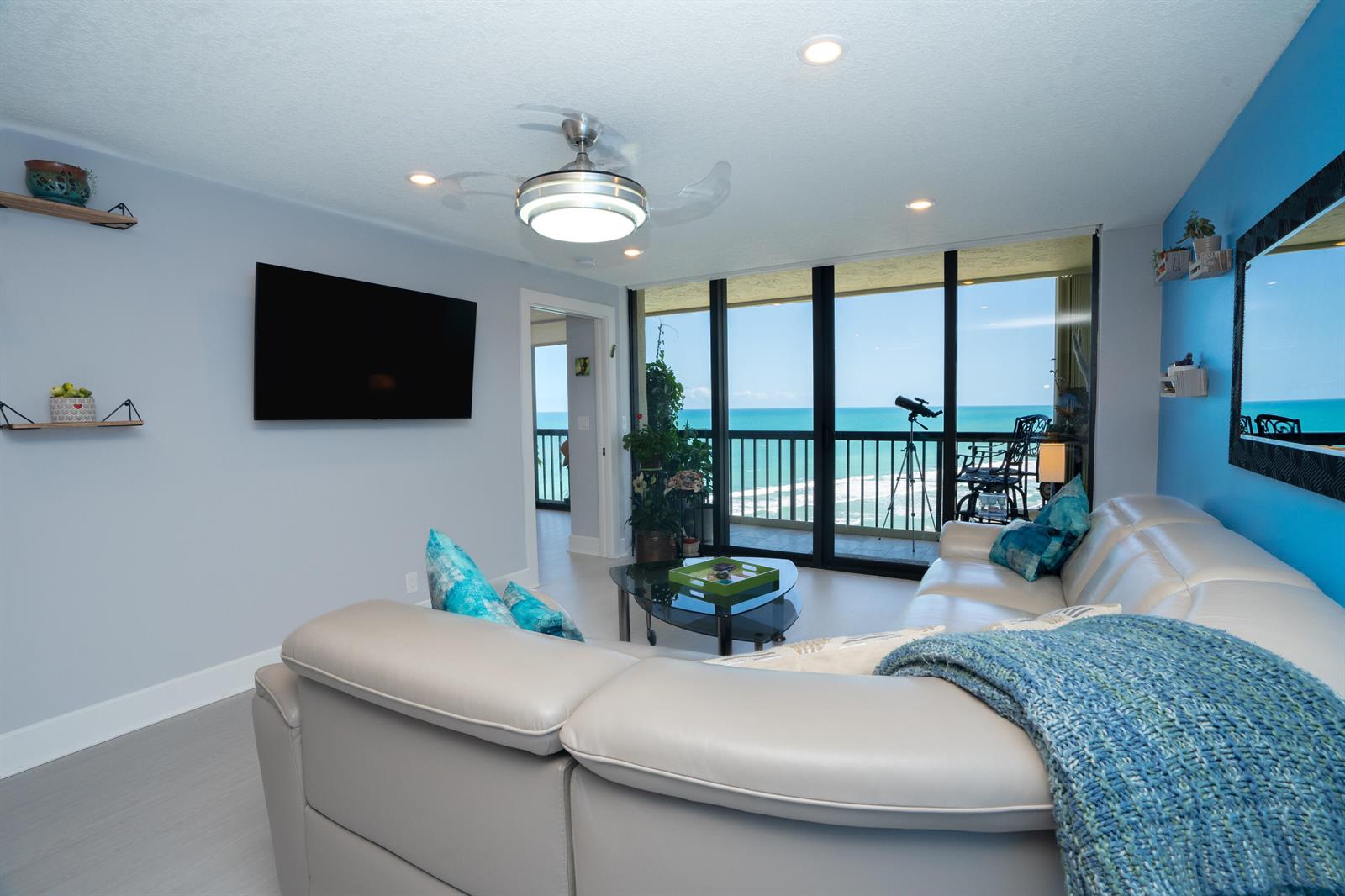 A living room with a white sectional sofa, a wall-mounted television, and floor-to-ceiling ocean views — 9500 S Ocean Drive # 1208, Jensen Beach FL 34957, JENSEN BEACH, FL