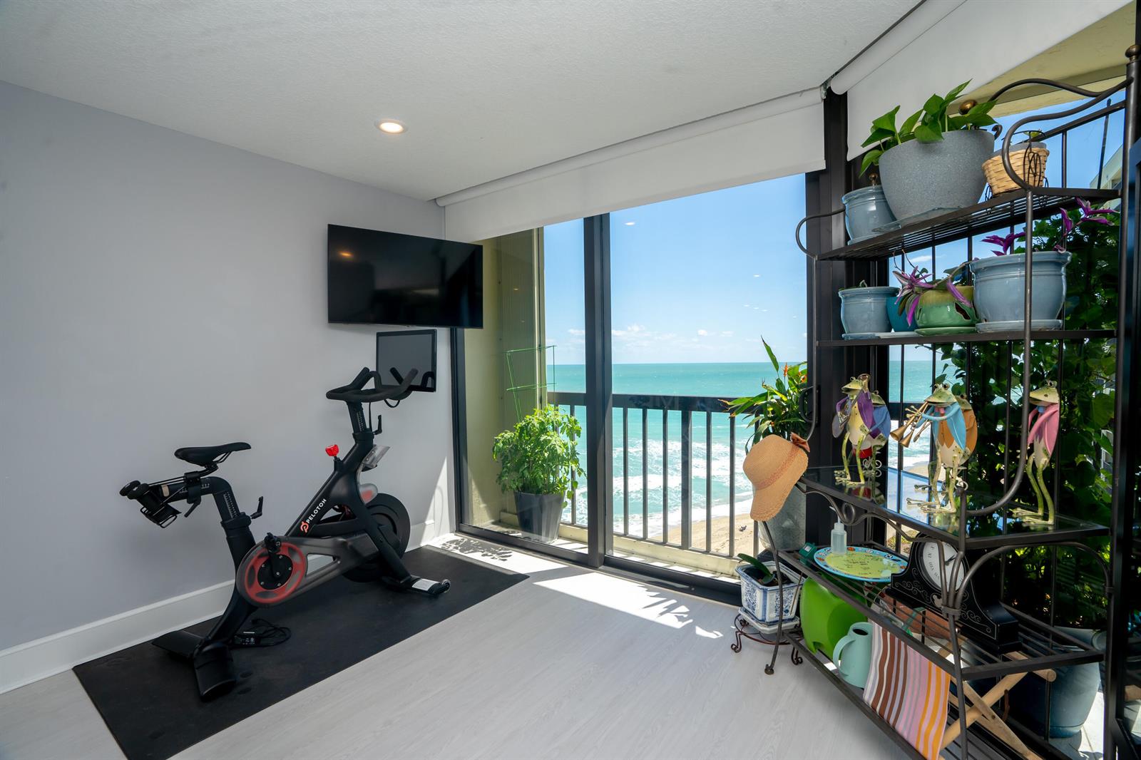 A home gym with a Peloton bike, wall-mounted television, and a balcony overlooking the ocean — 9500 S Ocean Drive # 1208, Jensen Beach FL 34957, JENSEN BEACH, FL