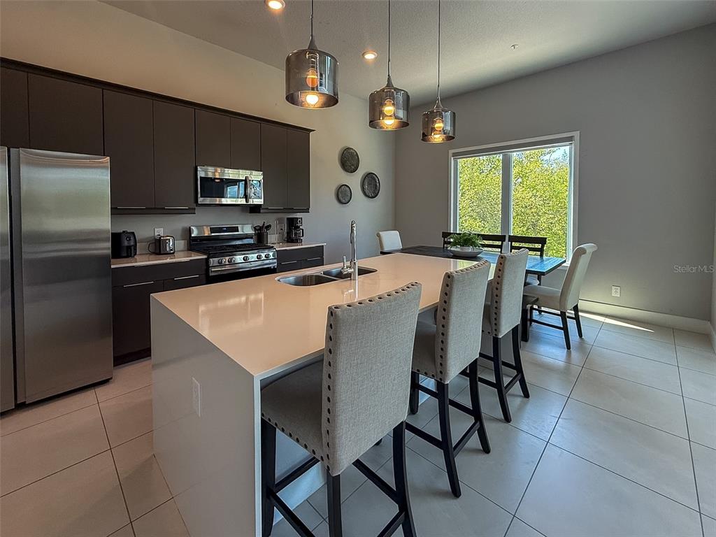 A modern kitchen features dark cabinetry, a large white island with bar seating, and pendant lights — 7770 SANDY RIDGE DRIVE UNIT 224, KISSIMMEE, FL