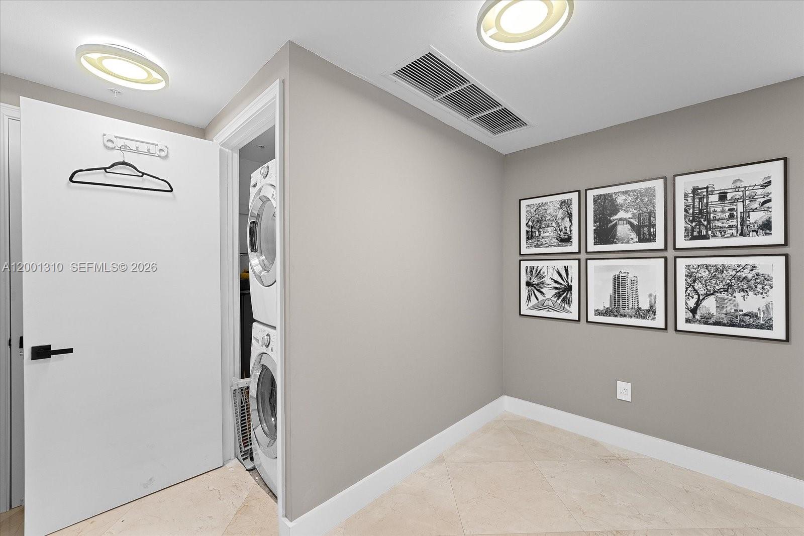 A laundry closet with a stacked washer and dryer sits beside a wall with framed art — 3400 SW 27th Ave # 201, Miami FL 33133, MIAMI, FL