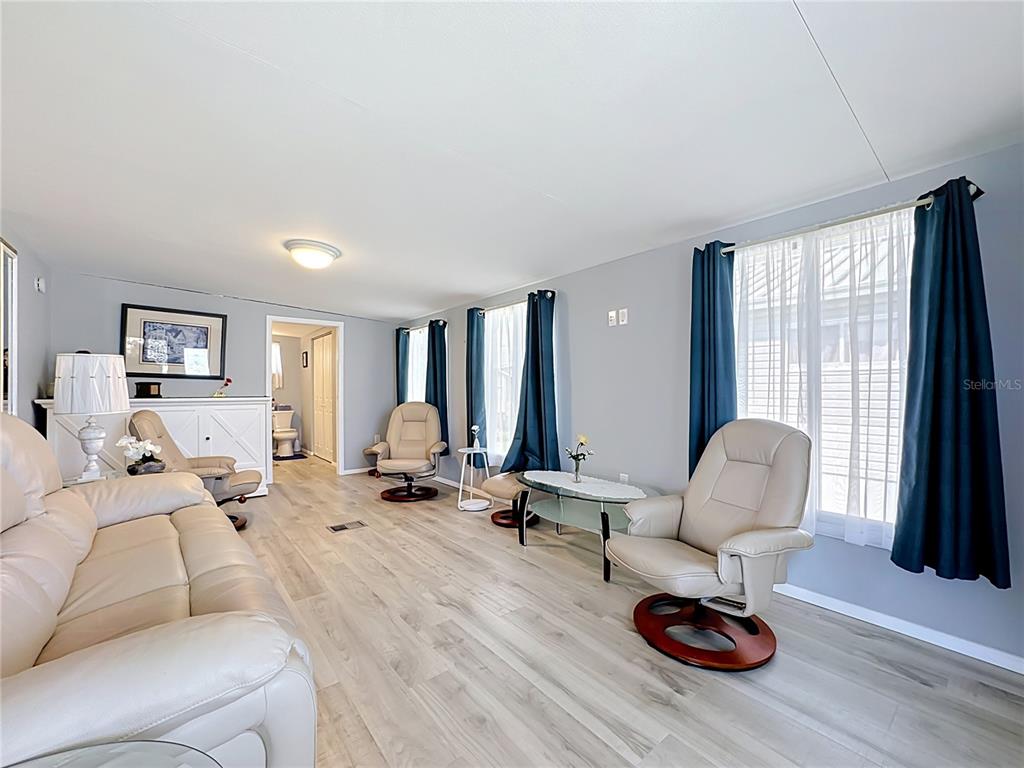 A living room features light wood-look flooring, beige leather recliners, and blue curtains — 3333 26TH AVENUE E UNIT 1222, BRADENTON, FL