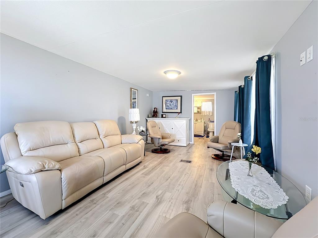 A living room features light wood-look flooring, a beige leather sofa, and two matching recliners — 3333 26TH AVENUE E UNIT 1222, BRADENTON, FL