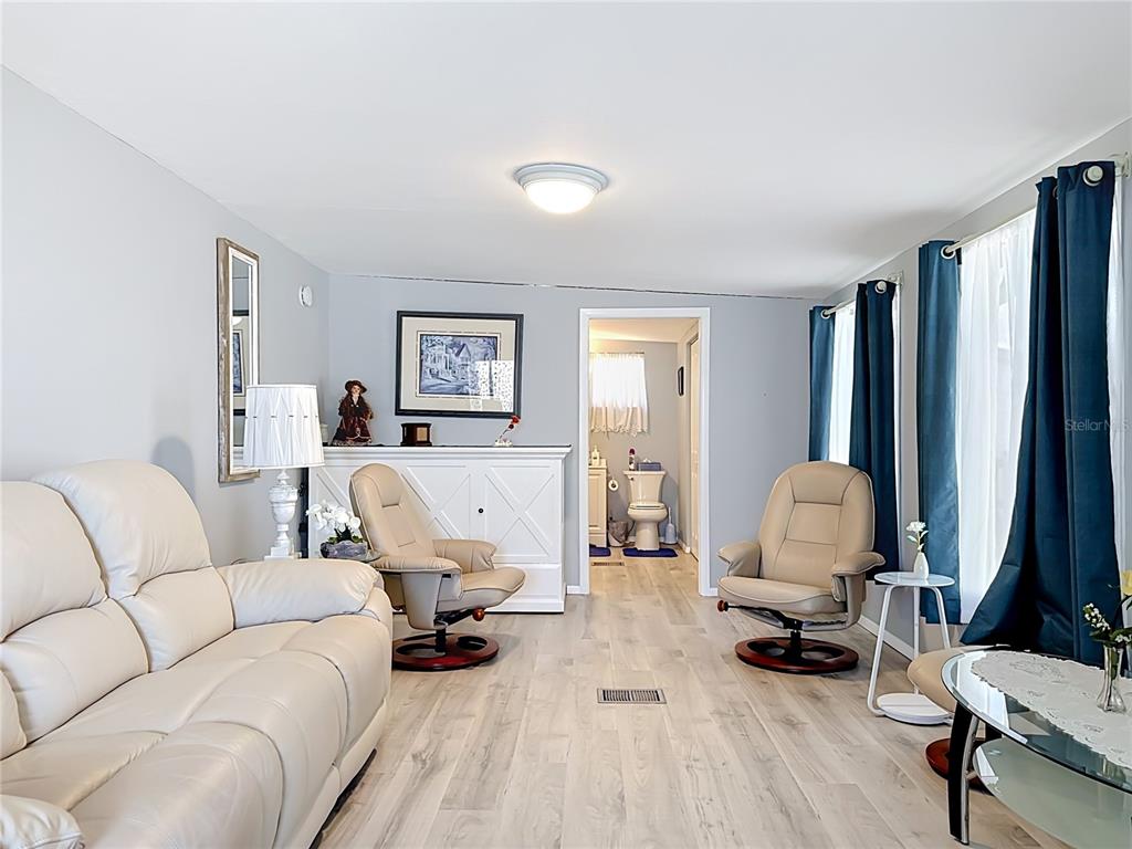 A living room with light wood flooring, beige leather furniture, and a view into a bathroom — 3333 26TH AVENUE E UNIT 1222, BRADENTON, FL