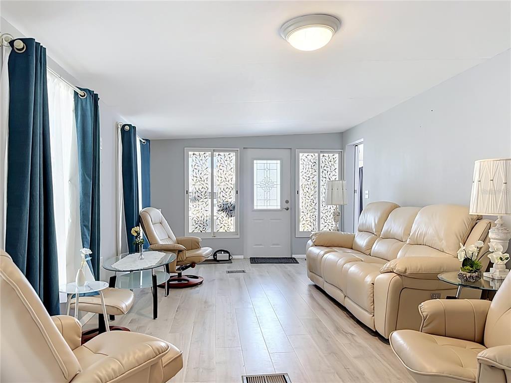A living room features light wood-look flooring, a beige leather sofa, and blue curtains — 3333 26TH AVENUE E UNIT 1222, BRADENTON, FL