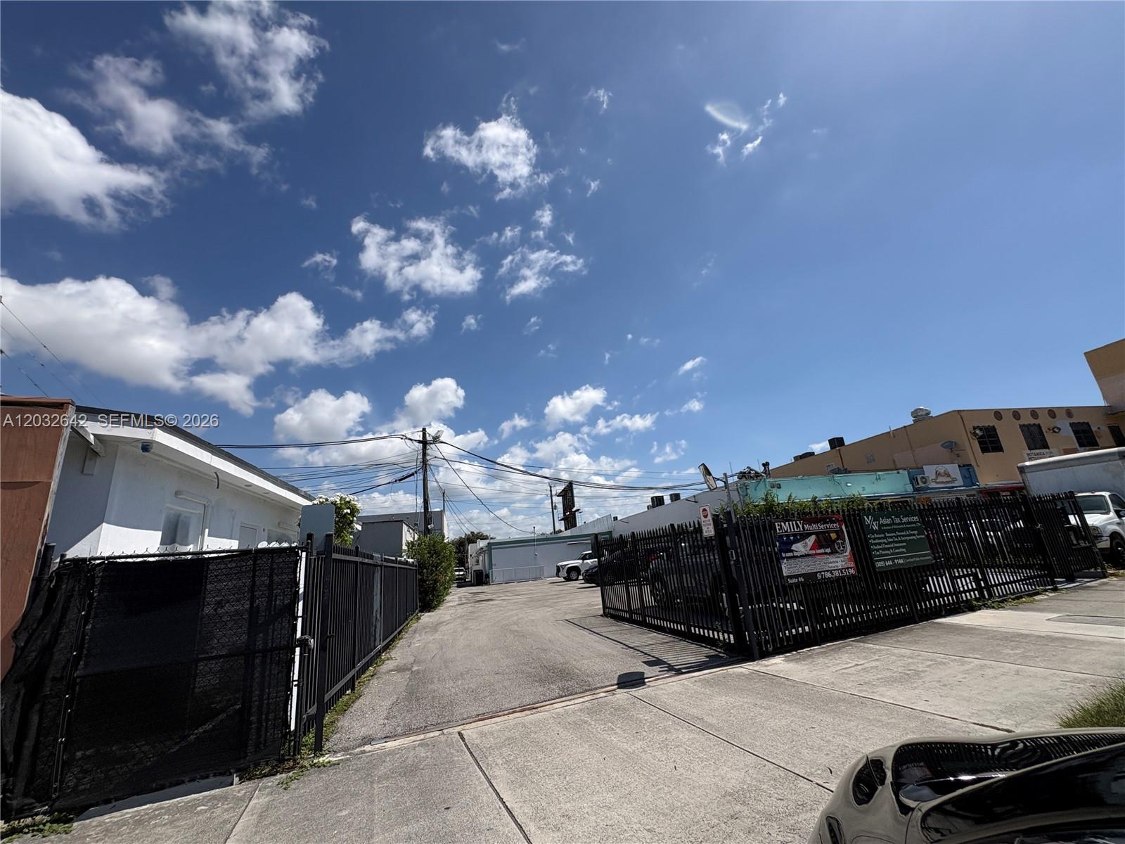 A paved driveway leads between two fenced commercial buildings under a bright blue sky — 1772 W Flagler St, Miami FL 33135, MIAMI, FL