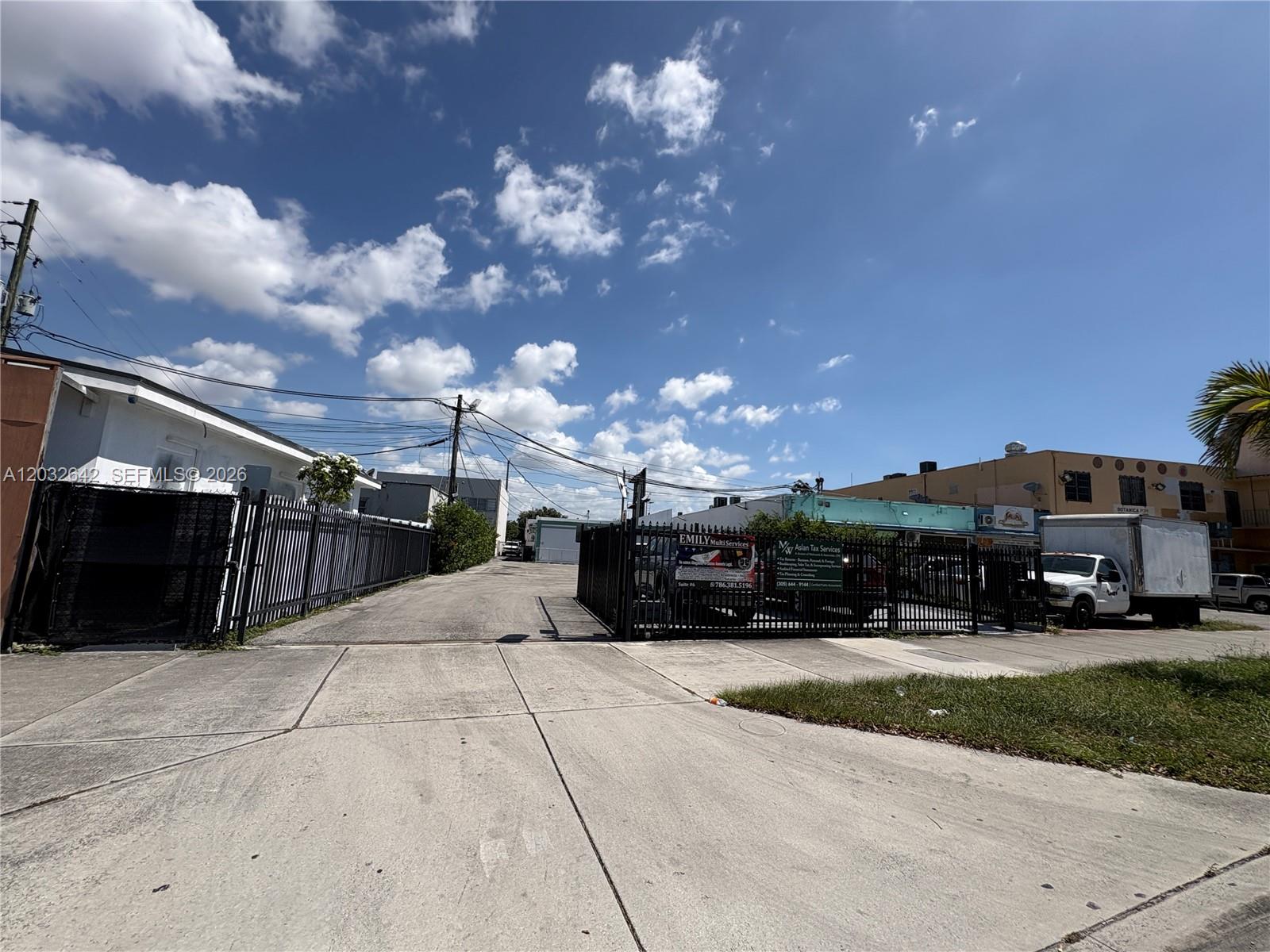 A paved driveway leads to a gated parking area between two commercial buildings under a sky — 1772 W Flagler St, Miami FL 33135, MIAMI, FL