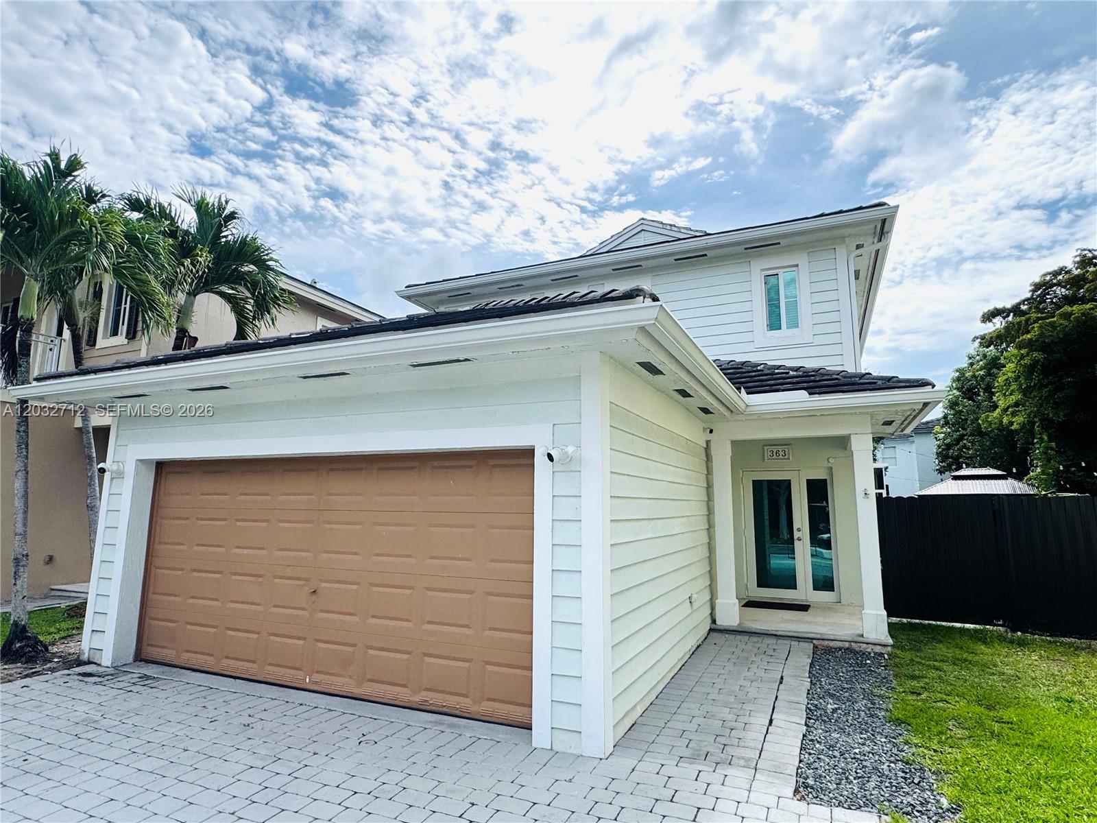 A two-story house features a tan garage door, light siding, and a paved walkway — 363 NE 35th Ter, Homestead FL 33033, HOMESTEAD, FL