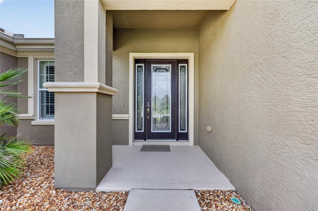 A covered entryway features a dark front door with glass panels and a concrete porch — 7419 SW 97TH TERRACE ROAD, OCALA, FL