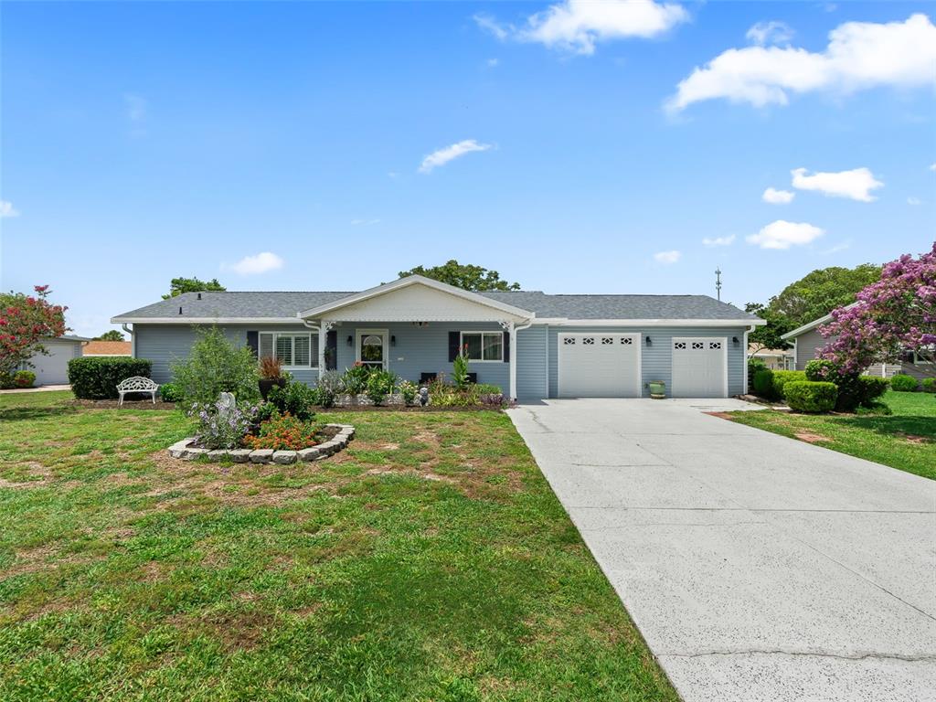 A single-story blue house features a concrete driveway, a two-car garage, and a front garden — 17584 SE 105TH TERRACE, SUMMERFIELD, FL