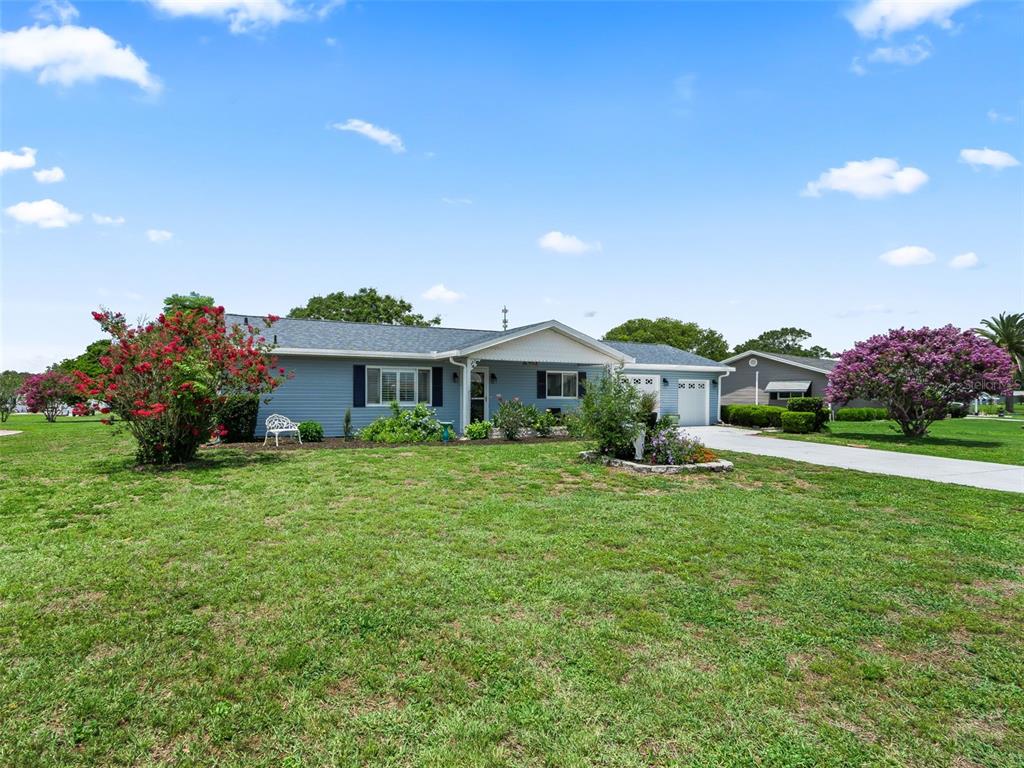 A light blue single-story house with a front lawn, driveway, and flowering trees — 17584 SE 105TH TERRACE, SUMMERFIELD, FL