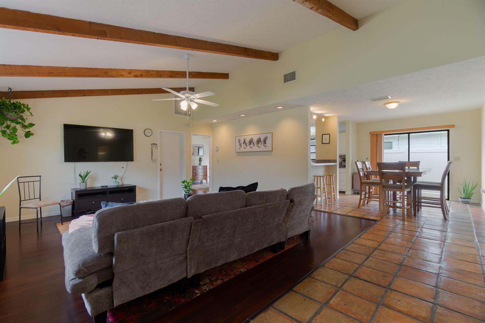 A living room with wood beams, a gray sofa, and tile flooring leading to a dining area — 6130 Francis Street, Jupiter FL 33458, JUPITER, FL