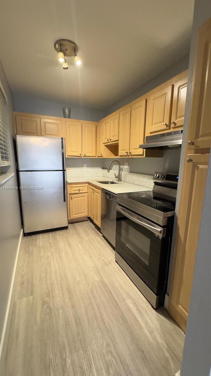 A galley kitchen features light wood cabinets, stainless steel appliances, and light-colored wood-look flooring — 1421 NW 45th St # 5, Deerfield Beach FL 33064, DEERFIELD BEACH, FL