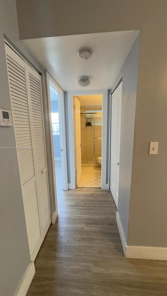 A hallway with wood-look flooring leads to a bathroom with a tiled shower — 1421 NW 45th St # 5, Deerfield Beach FL 33064, DEERFIELD BEACH, FL
