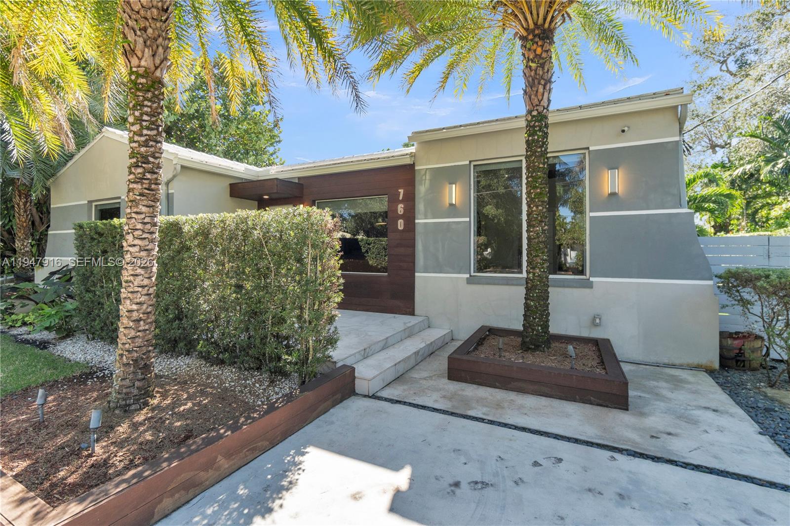 A modern house exterior features a wood-paneled entrance, gray walls, and a palm tree planter — 760 NE 115th St, Biscayne Park FL 33161, BISCAYNE PARK, FL