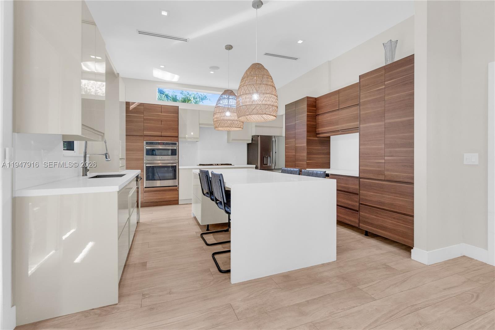 A modern kitchen features a white island, wood-grain cabinetry, and two woven pendant lights — 760 NE 115th St, Biscayne Park FL 33161, BISCAYNE PARK, FL