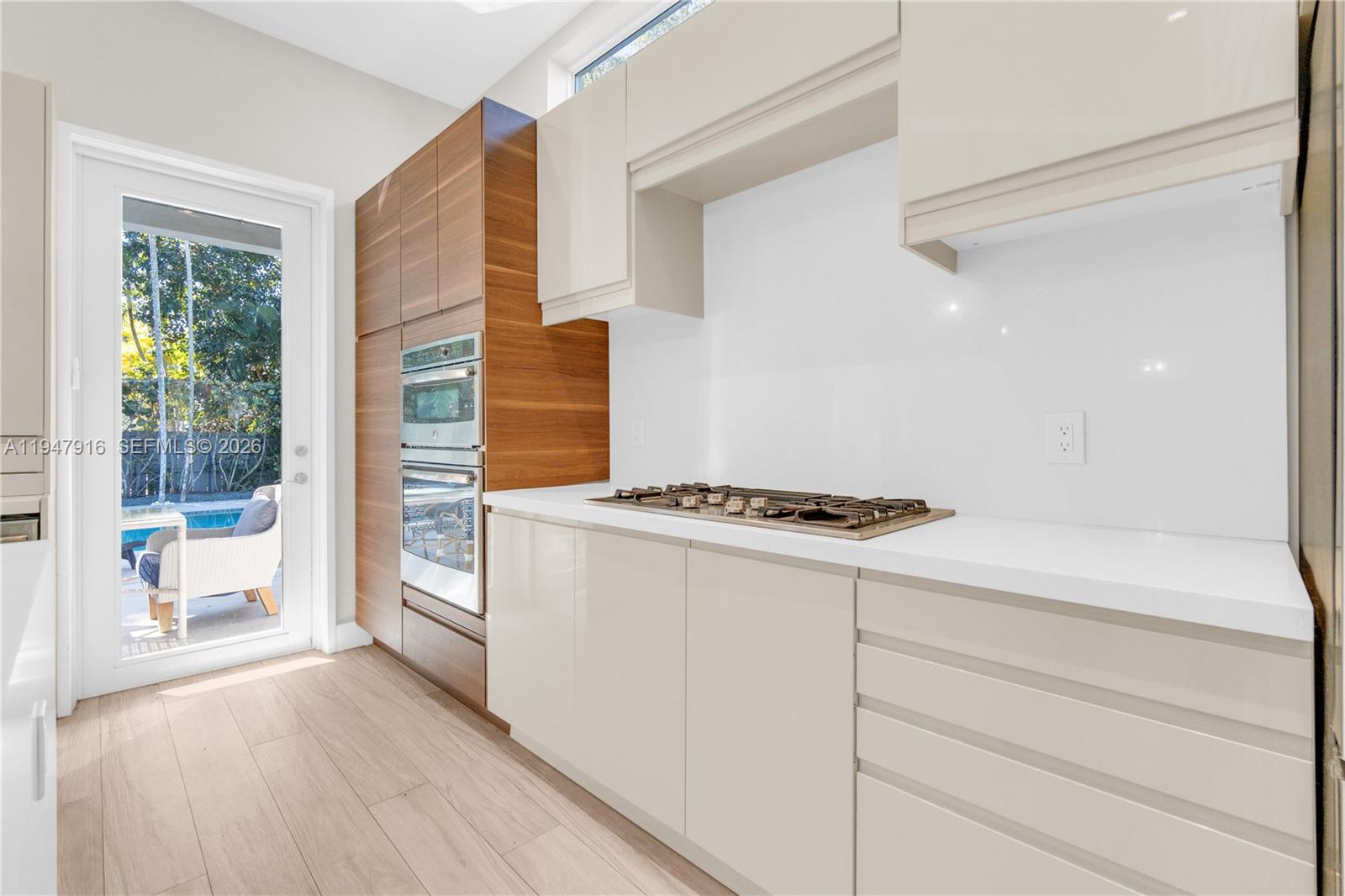 A modern kitchen features wood-grain cabinetry, light-colored lower cabinets, a gas cooktop, and glass doors — 760 NE 115th St, Biscayne Park FL 33161, BISCAYNE PARK, FL
