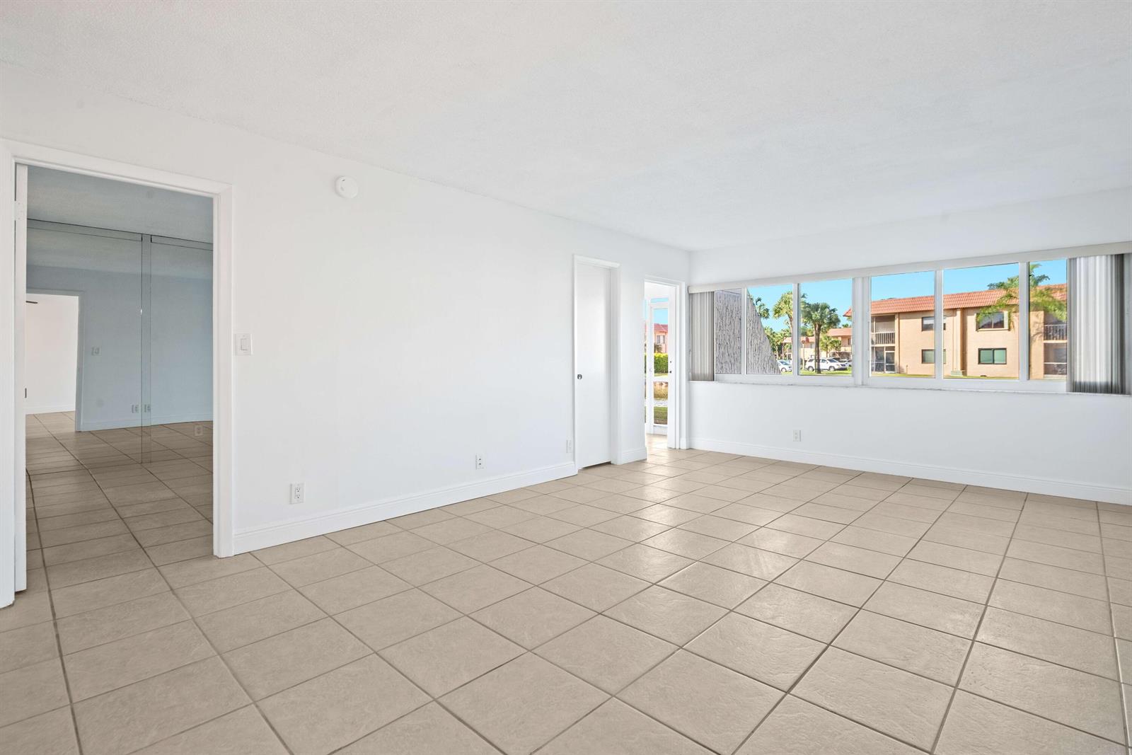 An empty room with white walls, beige tile flooring, and a large window overlooking buildings — 140 Lakeview Drive # 103, Weston FL 33326, WESTON, FL