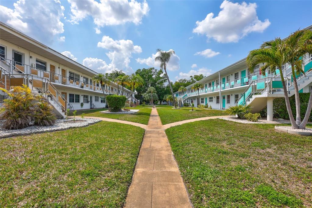 A concrete walkway leads between two two-story apartment buildings with exterior staircases and palm trees — 5940 21ST STREET N UNIT 11, ST PETERSBURG, FL