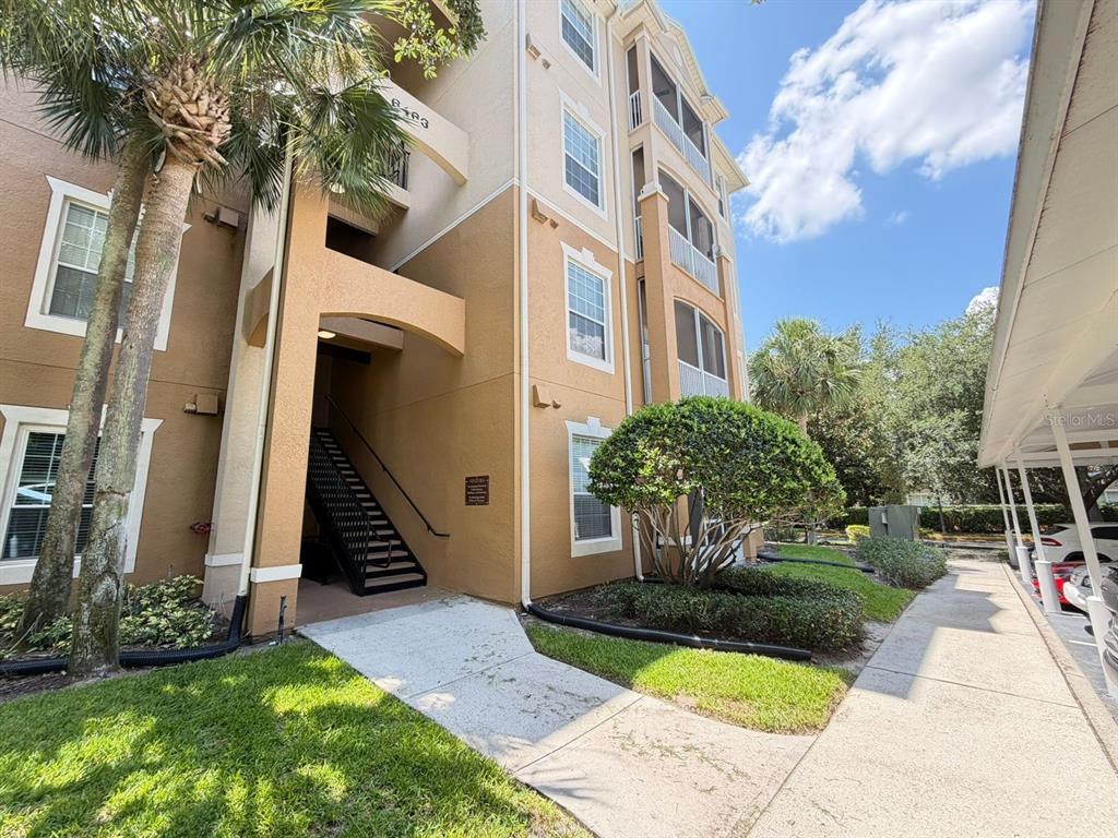 A multi-story apartment building exterior features tan stucco walls, a staircase, and a covered walkway — 6466 CAVA ALTA DRIVE UNIT 108, ORLANDO, FL